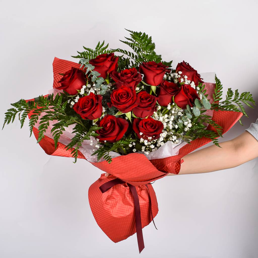 A Dozen Vibrant Red Roses Wrapped In Red Floral Paper