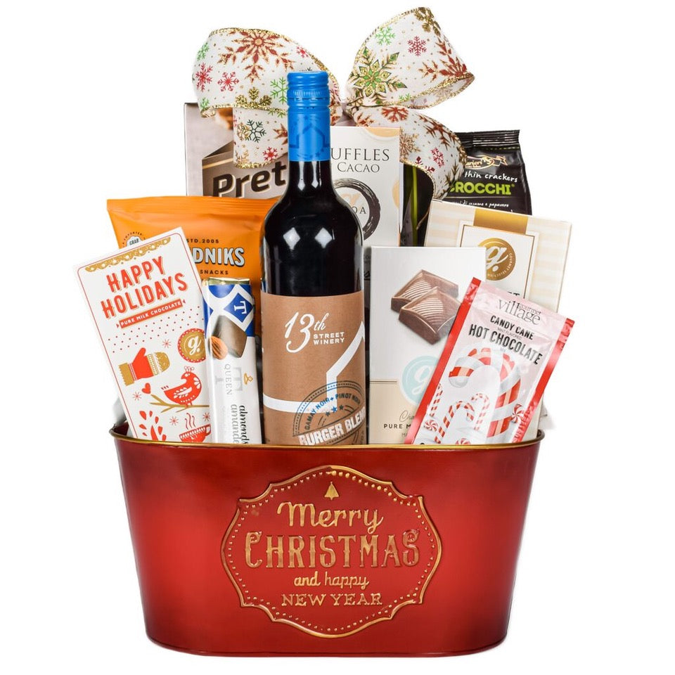 Red Merry Christmas Basket With Sweet And Savoury Items. Pretzels, Chocolate Truffles, Caramel Popcorn, Hot Cocoa Powder, And Ontario Red Wine