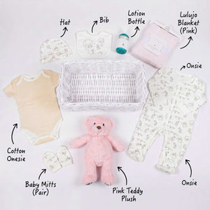 A flat layout of items include in the baskets: Hat, bib, lotion bottle, pink lulujo blanket, onsie, pink Teddy plush, baby mits and cotton onsie