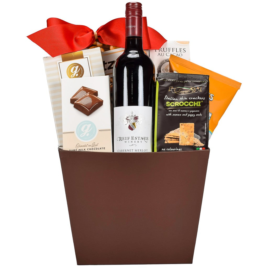 Brown Gift Basket With Red Bow Sweet And Savoury Items Including Pretzels, Milk Chocolate, Cookies, Crackers, Popcorn And Canadian Merlot Wine